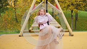 Happy child is riding a swing. Look into the camera and laugh. The girl flies on bungee. Cheerful childhood. Walk in