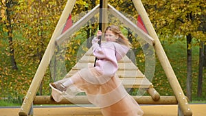 Happy child is riding a swing. Look into the camera and laugh. The girl flies on bungee. Cheerful childhood. Walk in