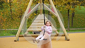 Happy child is riding a swing. Look into the camera and laugh. The girl flies on bungee. Cheerful childhood. Walk in