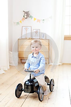 Happy child riding toy vintage car. Funny kid playing at home. Summer vacation and travel concept. Active little boy driving a car