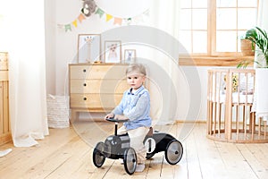 Happy child riding toy vintage car. Funny kid playing at home. Summer vacation and travel concept. Active little boy driving a car