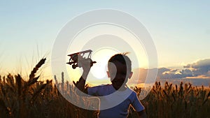 A happy child is running across a wheat field during sunset, holding a toy plane. The boy shows the flight of the