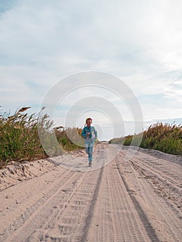 Happy child running jumping having fun on empty autumn beach. Blond girl walking on white sand road