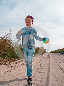 Happy child running jumping having fun on empty autumn beach. Blond girl walking on white sand road