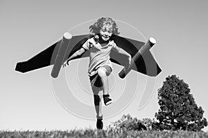 Happy child running with paper wings jumping against blue sky. Portrait of boy playing with toy jetpack. Freedom