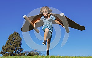 Happy child running with paper wings jumping against blue sky. Portrait of boy playing with toy jetpack. Freedom