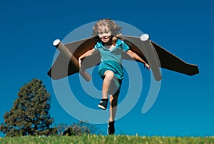 Happy child running with paper wings jumping against blue sky. Portrait of boy playing with toy jetpack. Freedom