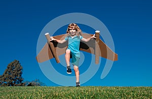 Happy child running with paper wings jumping against blue sky. Portrait of boy playing with toy jetpack. Freedom