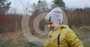 Happy Child Running In The Woods. Happy little boy playing in Park in autumn. Slow motion: The Boy in the Yellow Jacket