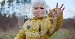 Happy Child Running In The Woods. Happy little boy playing in Park in autumn. Slow motion: The Boy in the Yellow Jacket