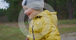 Happy Child Running In The Woods. Happy little boy playing in Park in autumn. Slow motion: The Boy in the Yellow Jacket