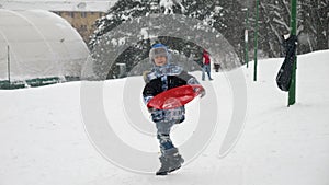 A happy child runs through the snow, sleds in hand, eager to reach the top of the hill for an exhilarating ride down.