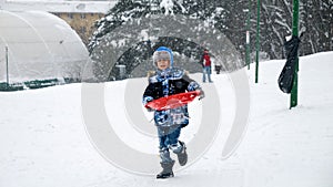 A happy child runs through the snow, sleds in hand, eager to reach the top of the hill for an exhilarating ride down