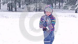 A happy child runs through a snowy forest during a snowfall in slow motion.