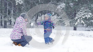A happy child runs to his mother and throws a snowball at her. Happy family in the forest or park on a beautiful winter