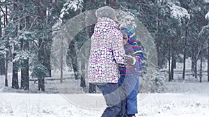 A happy child runs to his mother, who raises him above himself and kisses him on a winter snowy day during a snowfall