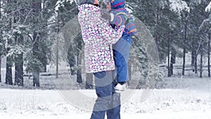 A happy child runs to his mother, who raises him up in the forest or in the park on a beautiful winter snowy day during