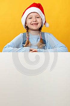 Happy child in santa hat is holding a blank space banner on a yellow background. Christmas card