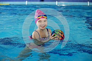 Happy child schoolgirl is studying at swimming lessons in pool. Swimming cap and goggles