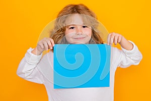 Happy child with sheet of paper, isolated on yellow background. Portrait of a kid holding a blank placard, poster. Empty