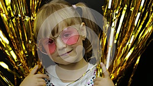 Happy child in shiny foil fringe golden curtain. Little blonde girl