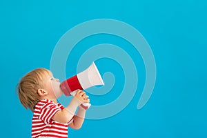 Happy child shouting by megaphone against blue background