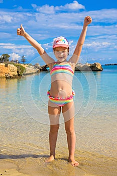 Happy child showing thumbs up on the beach.