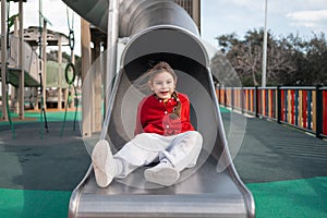 A happy child sits at the top of a slide in a playground, ready for fun and adventure