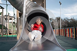 A happy child sits at the top of a slide in a playground, ready for fun and adventure