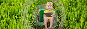 Happy child sitting on the field holding tablet. Boy sitting on the grass on sunny day. Home schooling or playing a