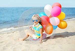 Happy child sitting on summer beach with colorful balloons