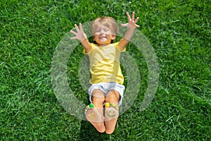 Happy child with smile on feet lying on green spring grass