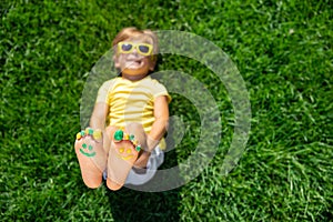 Happy child with smile on feet lying on green spring grass