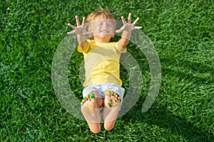 Happy child with smile on feet lying on green spring grass