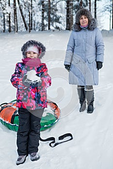 Happy child with snow in hands with mother at ski resort with toboggan