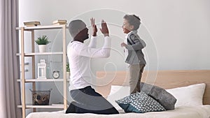 Happy child son jumping playing with black father on bed