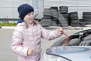 A happy child is standing next to a car with a wire in his hands.  Little girl works in the garage.  Repair service