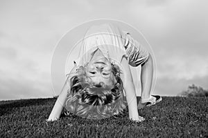 Happy child standing upside down on green grass. Laughing kid boy having fun in spring park. Healthy kids lifestyle