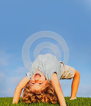 Happy child standing upside down on green grass. Laughing kid boy having fun in spring park. Healthy kids lifestyle