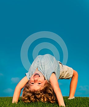Happy child standing upside down on green grass. Laughing kid boy having fun in spring park. Healthy kids lifestyle