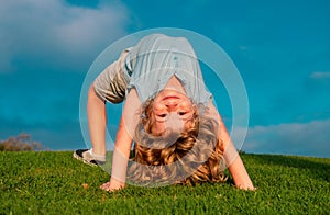Happy child standing upside down on green grass. Laughing kid boy having fun in spring park. Healthy kids lifestyle