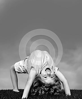 Happy child standing upside down on green grass. Laughing kid boy having fun in spring park. Healthy kids lifestyle