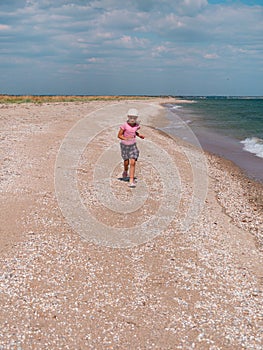 Happy child in a straw hat running jumping having fun on empty autumn sea beach. Blond girl walking on white sand