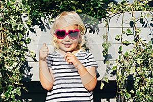 Happy child in summer sunglasses smiles looking at the camera and shows like with fingers.