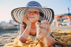 Happy child in swimsuit relaxing on the summer beach, lying on towel and playing with sand. Warm weather, cozy mood. Traveling on