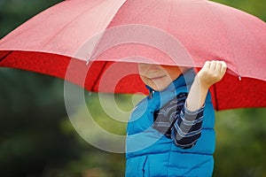 Happy child with an umbrella playing out in the rain in the summer outdoors. The boy smiles and hides his face under an umbrella