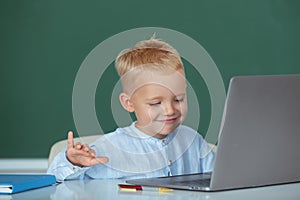 Happy child using gadgets to study. Computer education for kids. Funny blonde pupil on blackboard.