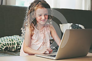 Happy child using laptop at home. School girl learning with computer and internet