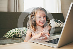 Happy child using laptop at home. School girl learning with computer and internet