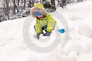 Happy child in warm clothing playing with snow. Child in warm clothing in winter. Kid making snowballs on winter cold day. Child p